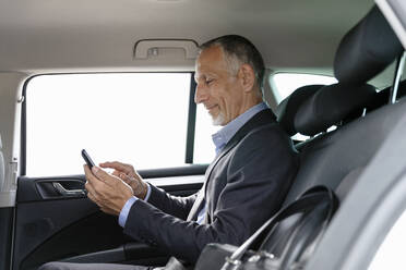 Businessman using smart phone while sitting on back seat in car - EIF01359