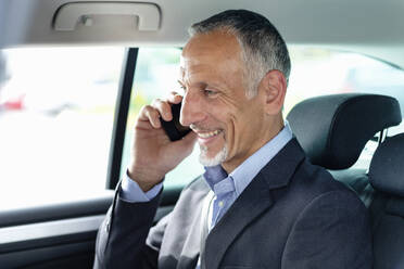 Smiling male business professional talking on mobile phone in car - EIF01369
