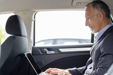 Geschäftsmann arbeitet im Auto sitzend am Laptop - EIF01370
