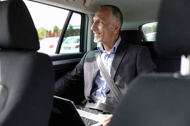Geschäftsmann schaut durch das Fenster, während er mit seinem Laptop im Auto sitzt - EIF01373