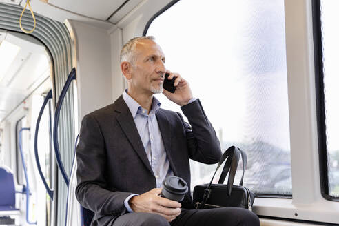 Geschäftsmann, der in der Straßenbahn sitzt und mit seinem Smartphone telefoniert - EIF01378