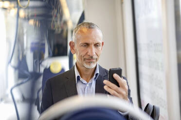 Male professional using smart phone while sitting in tram - EIF01379