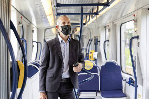 Geschäftsmann mit Schutzmaske in der Straßenbahn während einer Pandemie - EIF01383