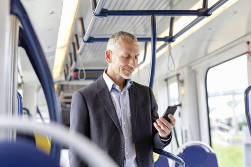 Männlicher Geschäftsmann, der ein Smartphone benutzt, während er in der Straßenbahn steht - EIF01384