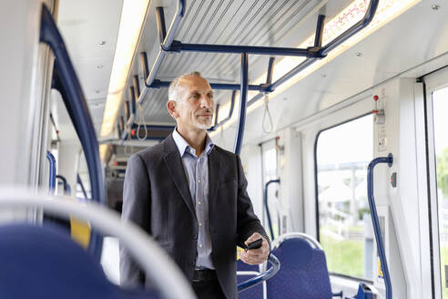 Männlicher Berufstätiger in Geschäftskleidung in der Straßenbahn stehend - EIF01385