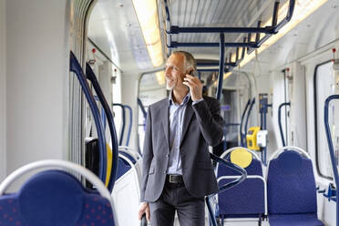Männlicher Geschäftsmann schaut weg, während er in der Straßenbahn mit seinem Smartphone telefoniert - EIF01388