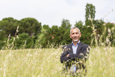 Male business professional with arms crossed standing in grassy field - EIF01395