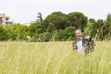 Smiling businessman holding briefcase while standing in field - EIF01396