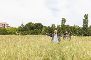 Happy businessman with arms outstretched standing in grassy field - EIF01397