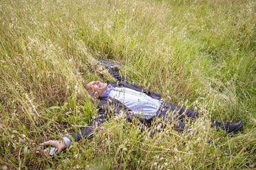 Smiling businessman lying down while relaxing on grassy field - EIF01399