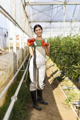 Lächelnde Bäuerin mit frischen roten Tomaten auf einem Biohof an einem sonnigen Tag - OIPF01059