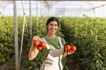 Lächelnde Landarbeiterin mit frischen roten Tomaten im Gewächshaus - OIPF01060