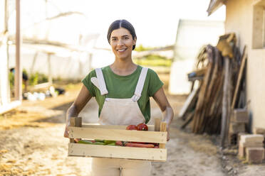 Smiling female farm worker standing with crate of vegetables - OIPF01061