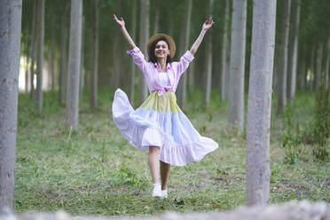 Lächelnde Frau tanzt mit erhobenen Armen im Wald - JSMF02344