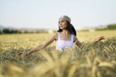 Junge schöne Frau mit Kopftuch steht in einem Weizenfeld und schaut weg - JSMF02347