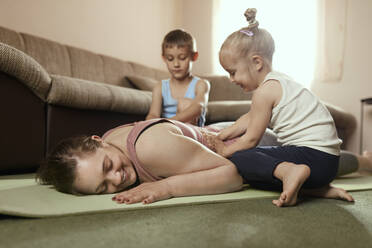 Son and daughter massaging mother's back on exercise mat at home - ZEDF04238