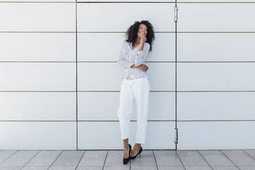 Smiling woman standing in front of wall looking away - JRVF01037