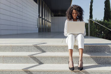 Female professional using laptop while sitting on steps during sunny day - JRVF01057