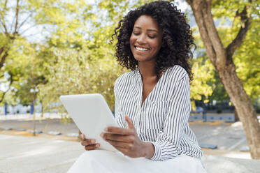 Fröhliche weibliche Fachkraft, die ein digitales Tablet benutzt, während sie im Büropark sitzt - JRVF01067
