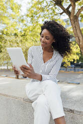 Smiling young businesswoman using digital tablet while sitting at office park - JRVF01068