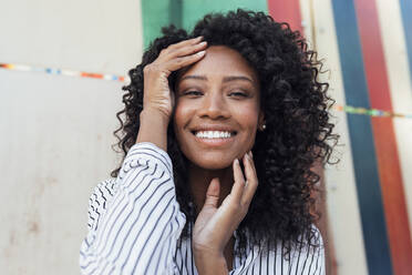 Lächelnde schöne Frau mit lockigem Haar vor einer Wand stehend - JRVF01101