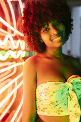 Smiling beautiful woman standing by neon lights - JRVF01140