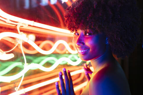 Lächelnde Afro-Frau, die Neonlichter berührt - JRVF01141