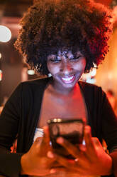 Smiling young woman using mobile phone in bar - JRVF01145