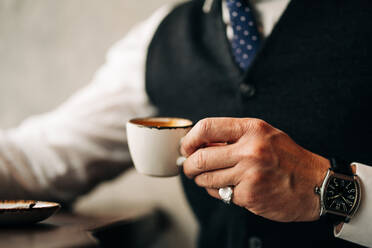 Bild eines anonymen männlichen Unternehmers in formeller Kleidung und Armbanduhr, der in einem Café ein heißes Getränk aus einer Tasse genießt - ADSF24815