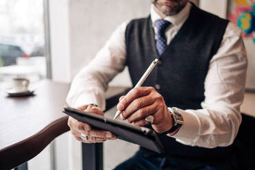 View of crop anonymous male executive using stylus and cellphone at cafeteria table - ADSF24824