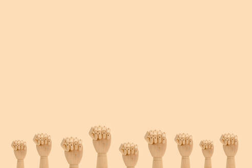Minimalistische Komposition von hölzernen Händen, die Fäuste als Symbol des Protests zeigen, vor einem beigen Hintergrund - ADSF24845