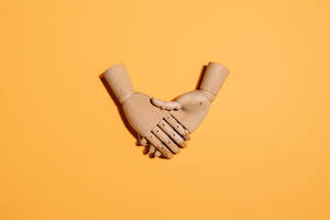 Top view of wooden hands demonstrating handshake as sign of agreement placed on yellow background - ADSF24847
