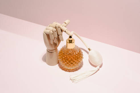 Stylish transparent bottle of perfume placed between wooden hand placed on pink background in light studio - ADSF24849