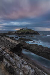 Atemberaubende Landschaft der felsigen Insel mit Leuchtturm im Meer in der Nähe von felsigen Küste in Faro Tapia de Casariego in Asturien in Spanien unter bewölktem Himmel bei Sonnenaufgang befindet - ADSF24859