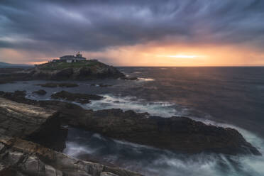 Atemberaubende Landschaft der felsigen Insel mit Leuchtturm im Meer in der Nähe von felsigen Küste in Faro Tapia de Casariego in Asturien in Spanien unter bewölktem Himmel bei Sonnenaufgang befindet - ADSF24860