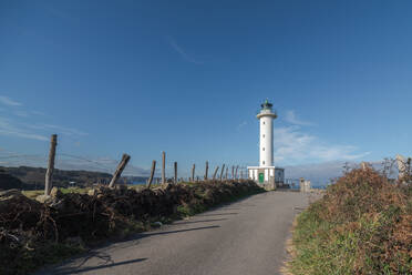 Asphaltstraße zum weißen Leuchtturm in Faro de Lastres in Asturien in Spanien unter wolkenlosem blauen Himmel bei Tag - ADSF24861