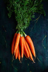 Top view of bunch of whole raw carrots with stems and leaves on wooden surface - ADSF24865