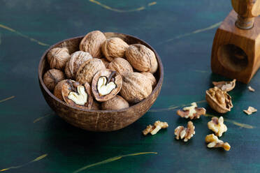 Round shaped wooden bowl full of crunchy walnuts with dry uneven nutshells on table - ADSF24868