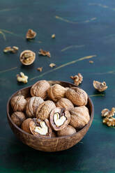 Round shaped wooden bowl full of crunchy walnuts with dry uneven nutshells on table - ADSF24869