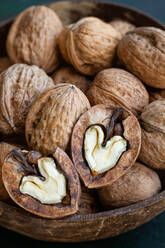 Round shaped wooden bowl full of crunchy walnuts with dry uneven nutshells on table - ADSF24870