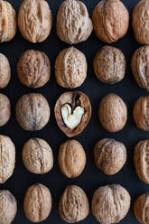 Top view of textured backdrop representing heart shaped walnut center among whole nuts with uneven nutshells - ADSF24871