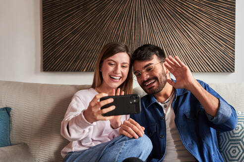 Romantisches junges Paar in legerer Kleidung, das sich auf dem Sofa entspannt und Fotos auf dem Smartphone anschaut, während des Wochenendes zu Hause - ADSF24908