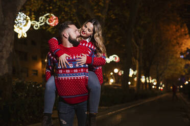 Man piggybacking woman during Christmas at night - LJF02184