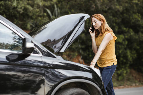 Rothaarige Frau, die mit ihrem Handy telefoniert und sich an ein Auto lehnt - LJF02191