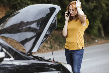 Verwirrte Frau kratzt sich am Kopf, während sie im Auto mit dem Handy telefoniert - LJF02192