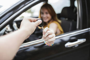 Hand giving key to woman sitting in car - LJF02194