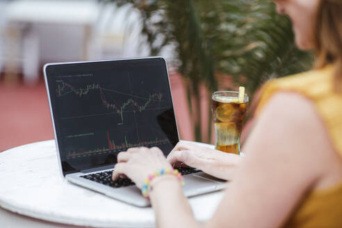 Woman trading on stock market through laptop at bar - LJF02198