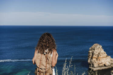 Weiblicher Backpacker mit Blick auf das Meer an einem sonnigen Tag - EBBF04040