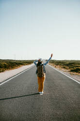 Backpacker waving hand while standing on road - EBBF04048