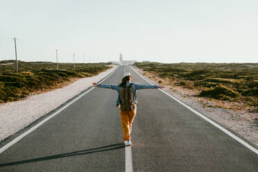 Carefree woman with arms outstretched walking on road marking - EBBF04050